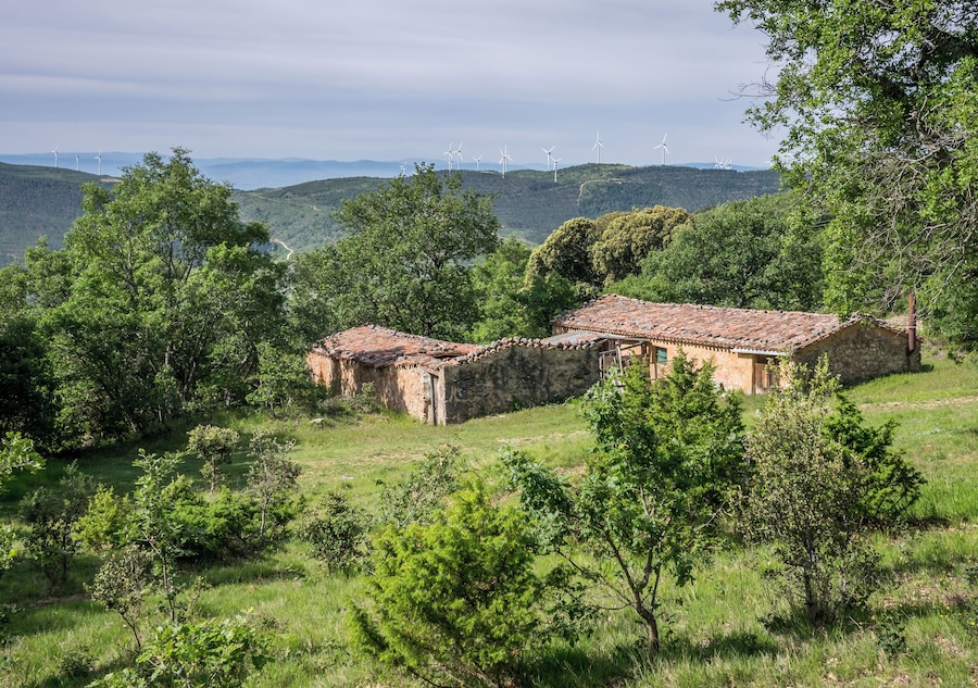 A stone house with a tiled roof surrounded by lush greenery and hills.