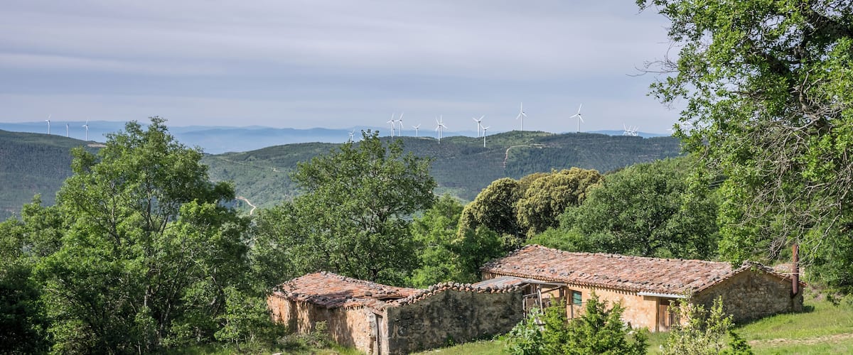A stone house with a tiled roof surrounded by lush greenery and hills.