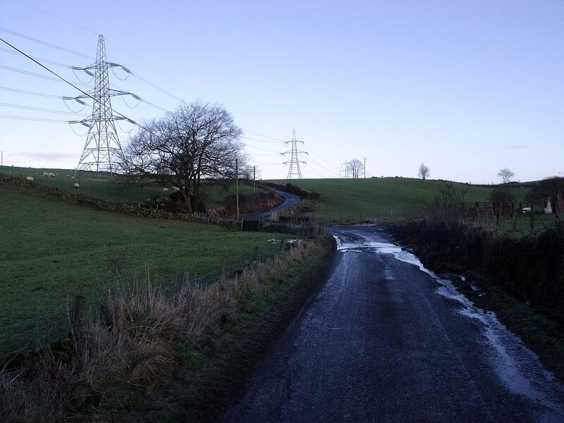 A rural road with a small stream, surrounded by grassy fields and power lines.