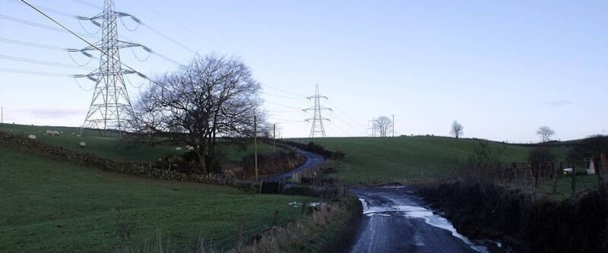 A rural road with a small stream, surrounded by grassy fields and power lines.