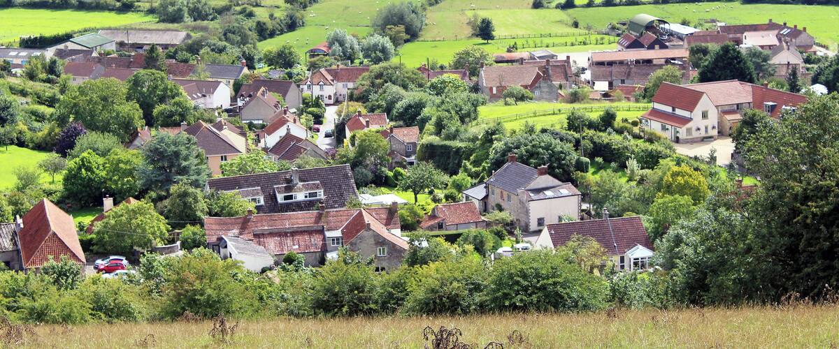 A rural village with houses, green fields, and rolling hills in the background.