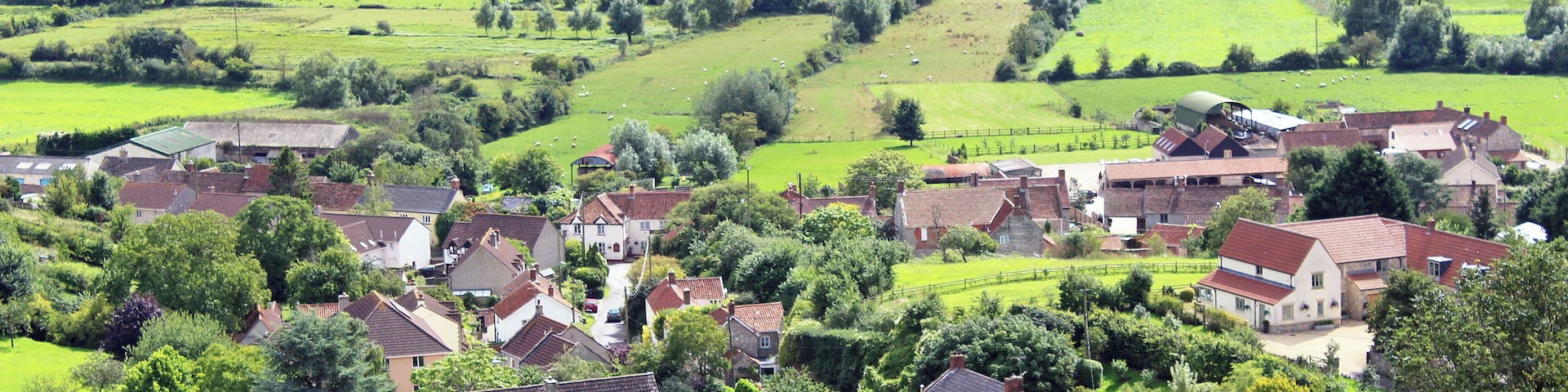 A rural village with houses, green fields, and rolling hills in the background.