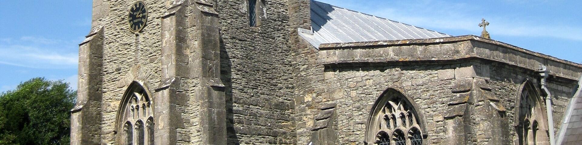 A historic stone church with a tall tower, arched windows, and a weather vane.