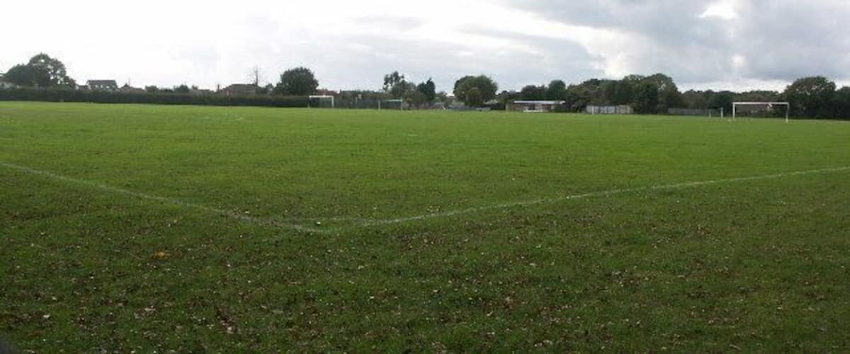 A large, open grassy field with a soccer goal in the distance and trees in the background.