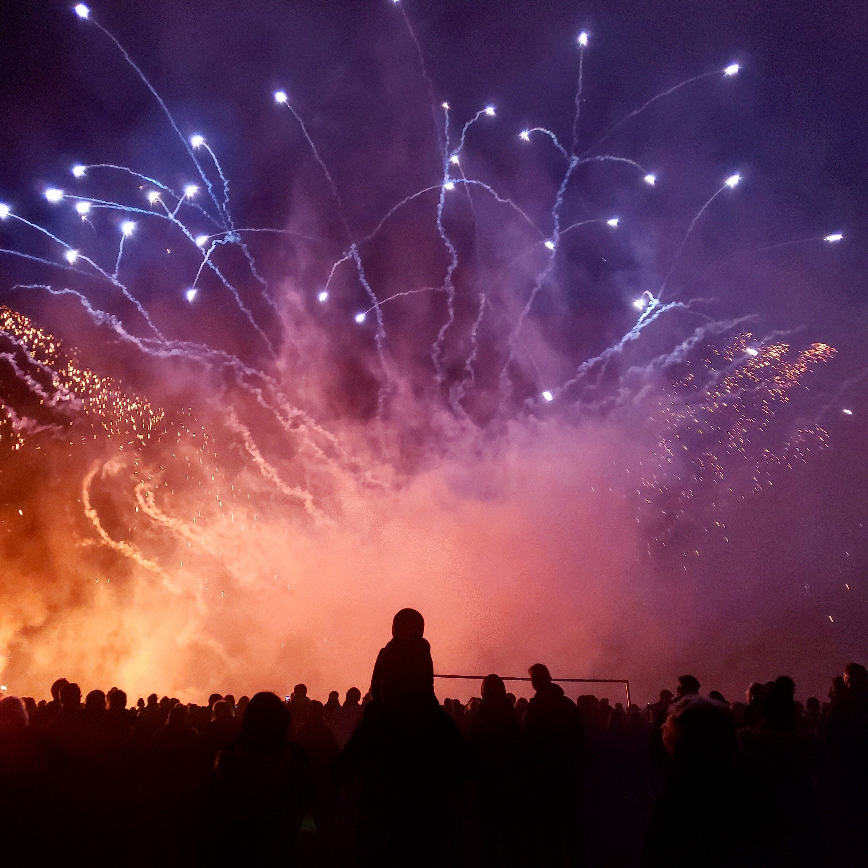 A crowd of people watching fireworks in the night sky.
