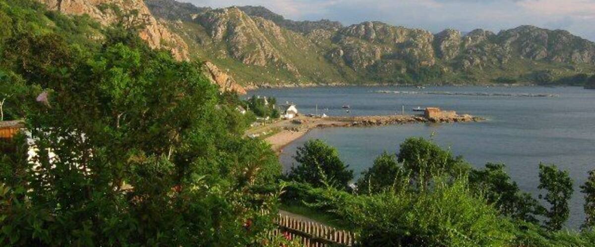 A coastal landscape with mountains, a beach, and a small settlement.