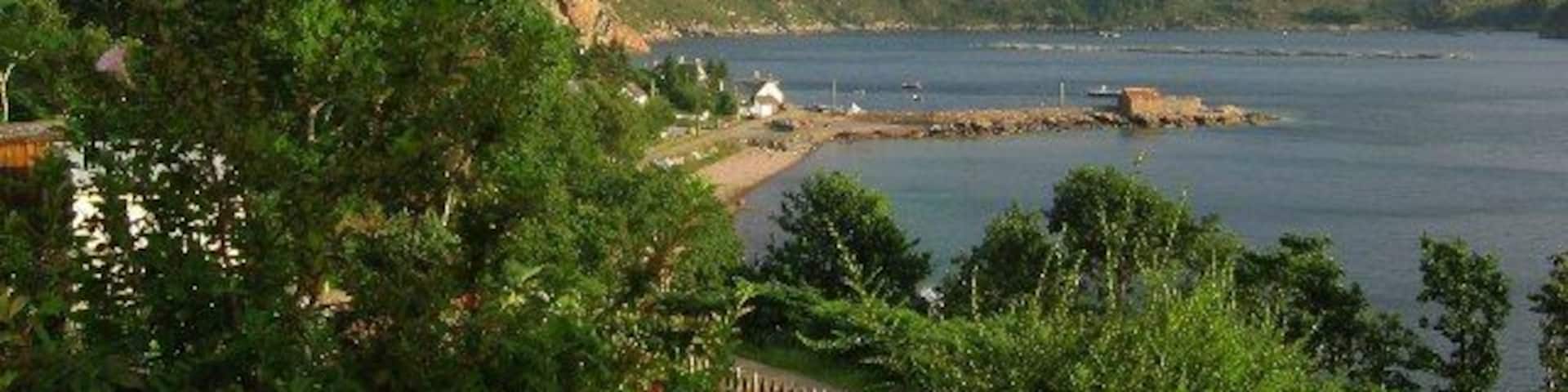 A coastal landscape with mountains, a beach, and a small settlement.