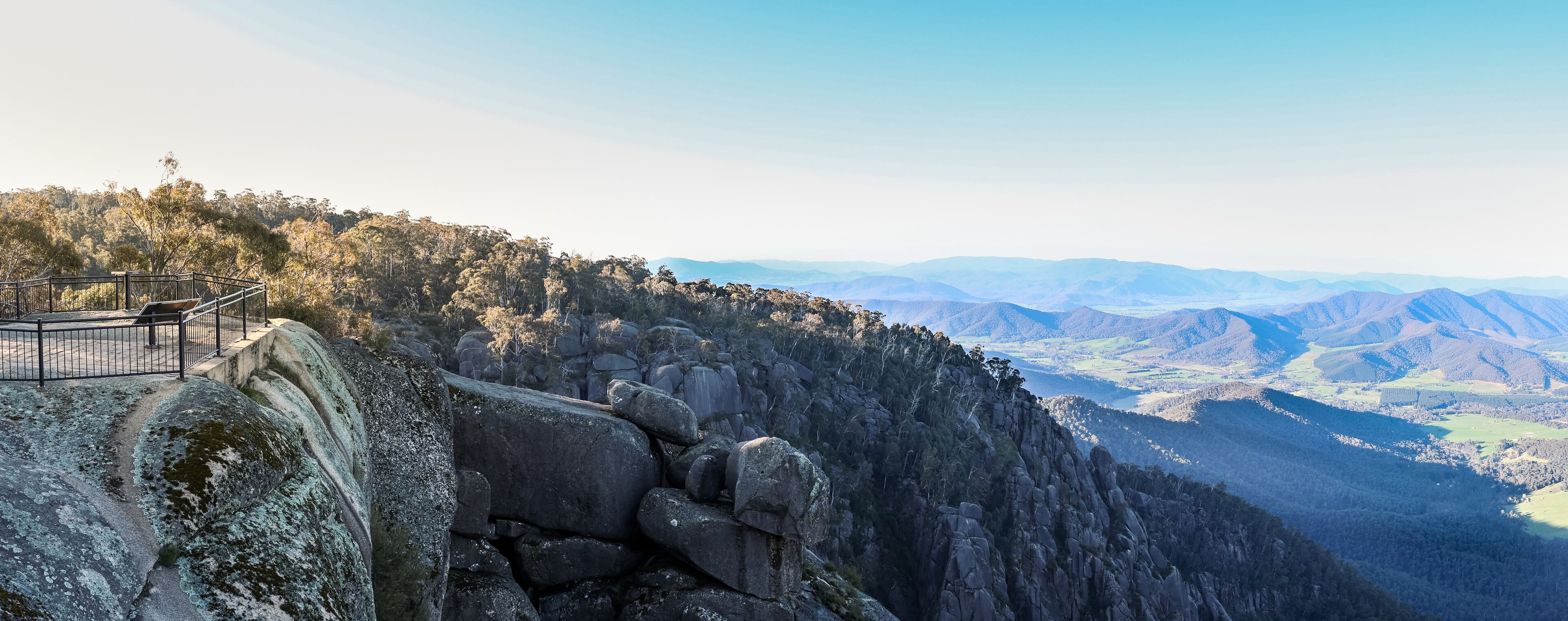 A rocky cliff with a viewing platform overlooking a valley.