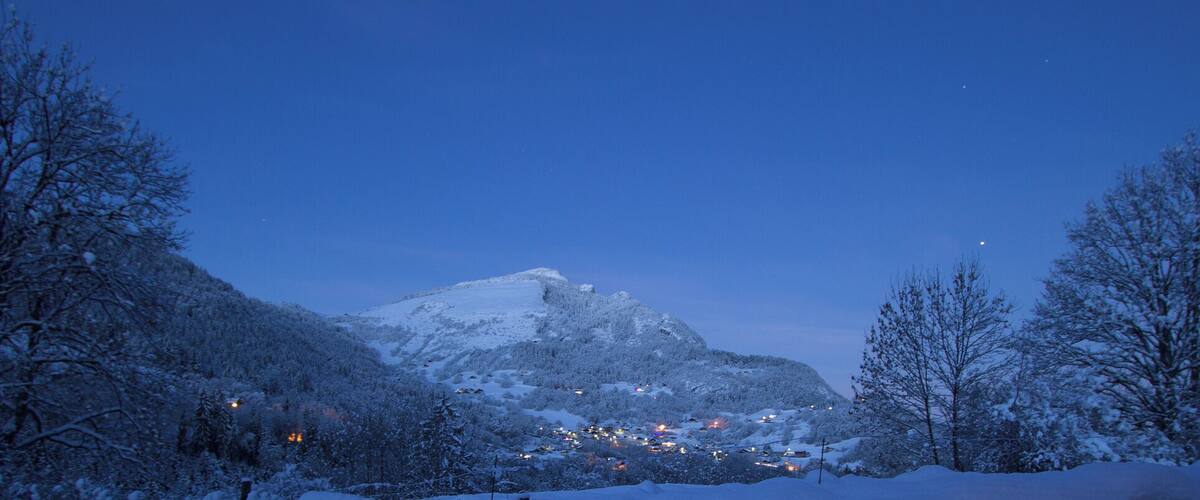 A snow-covered mountain at dusk with a small village at its base.
