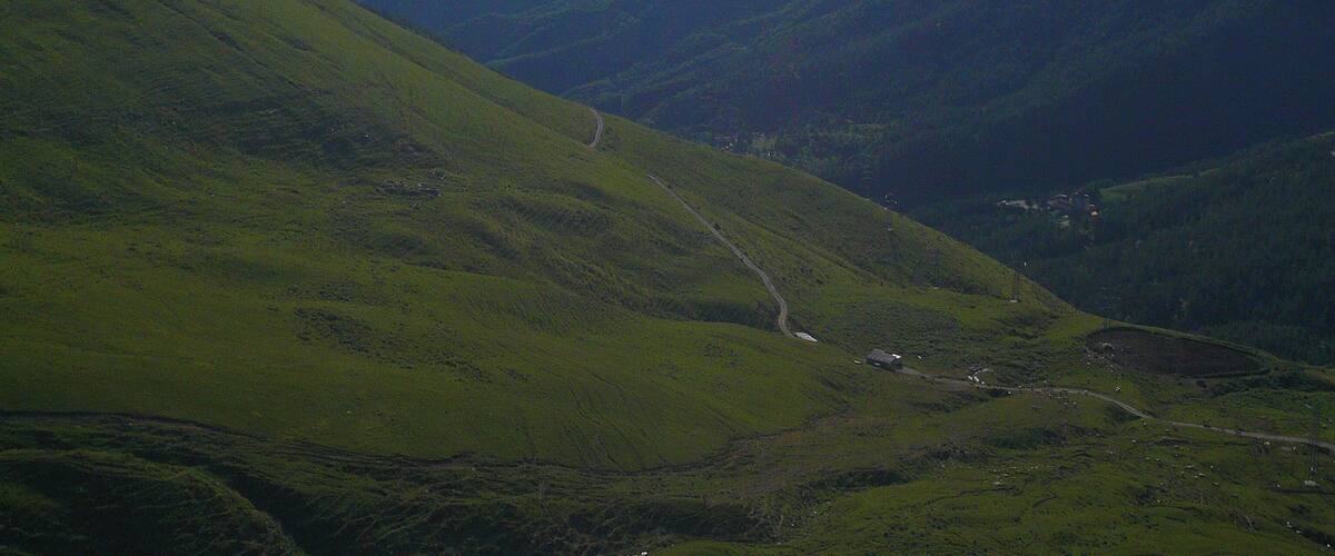 A valley with a winding road and a small house.