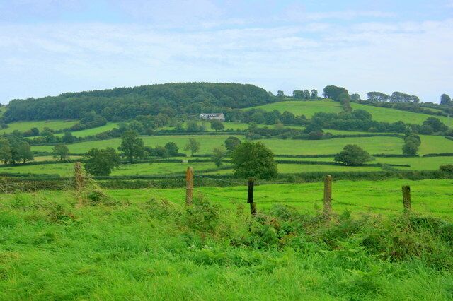 Rolling green hills, a wooden fence, and a distant house on a hill.
