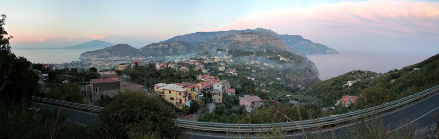 A coastal town with buildings on a hillside, a road, and a mountain in the background.