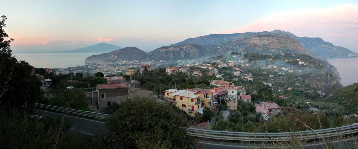 A coastal town with buildings on a hillside, a road, and a mountain in the background.