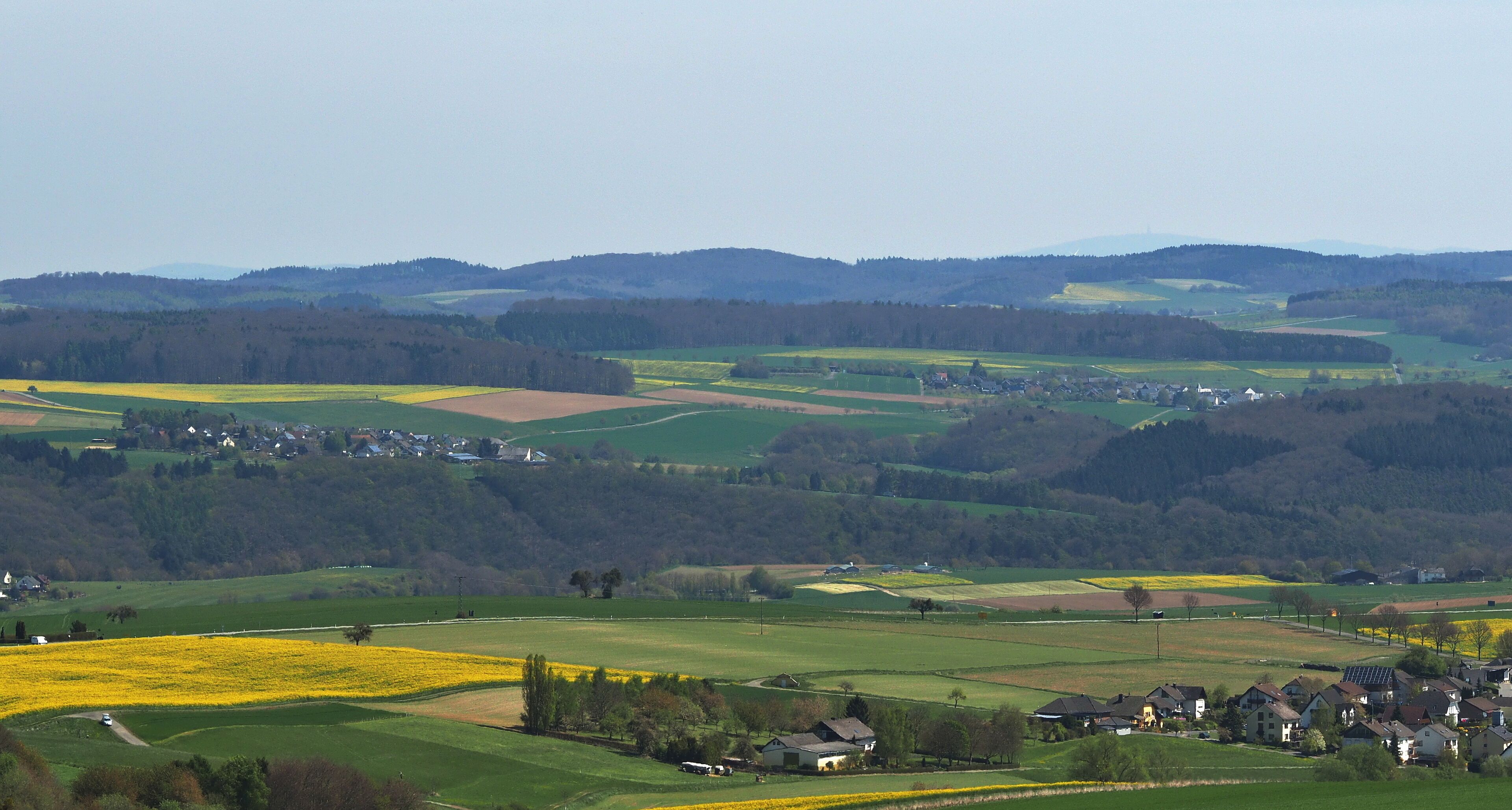 A rural landscape with fields, houses, and rolling hills.
