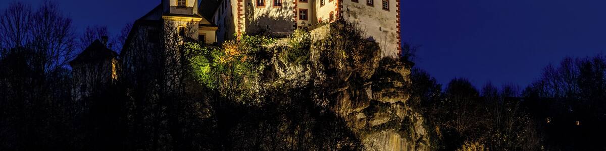 Eine Burg auf einem Felsen mit beleuchteten Fenstern und einem Glockenturm.
