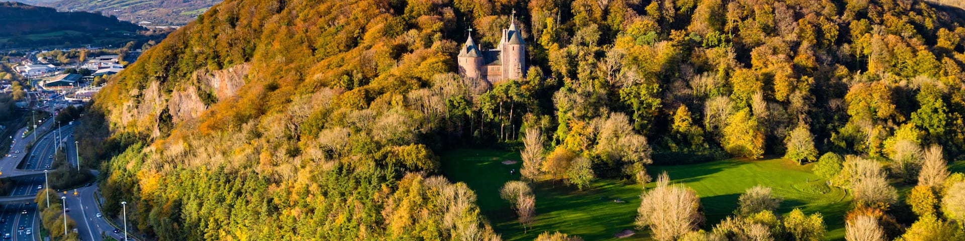 A castle surrounded by autumn foliage, a highway, and a small body of water.