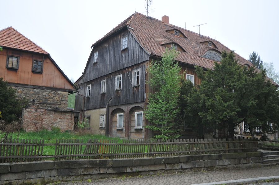 A historic building with a wooden facade and a tiled roof, surrounded by trees and a stone wall.