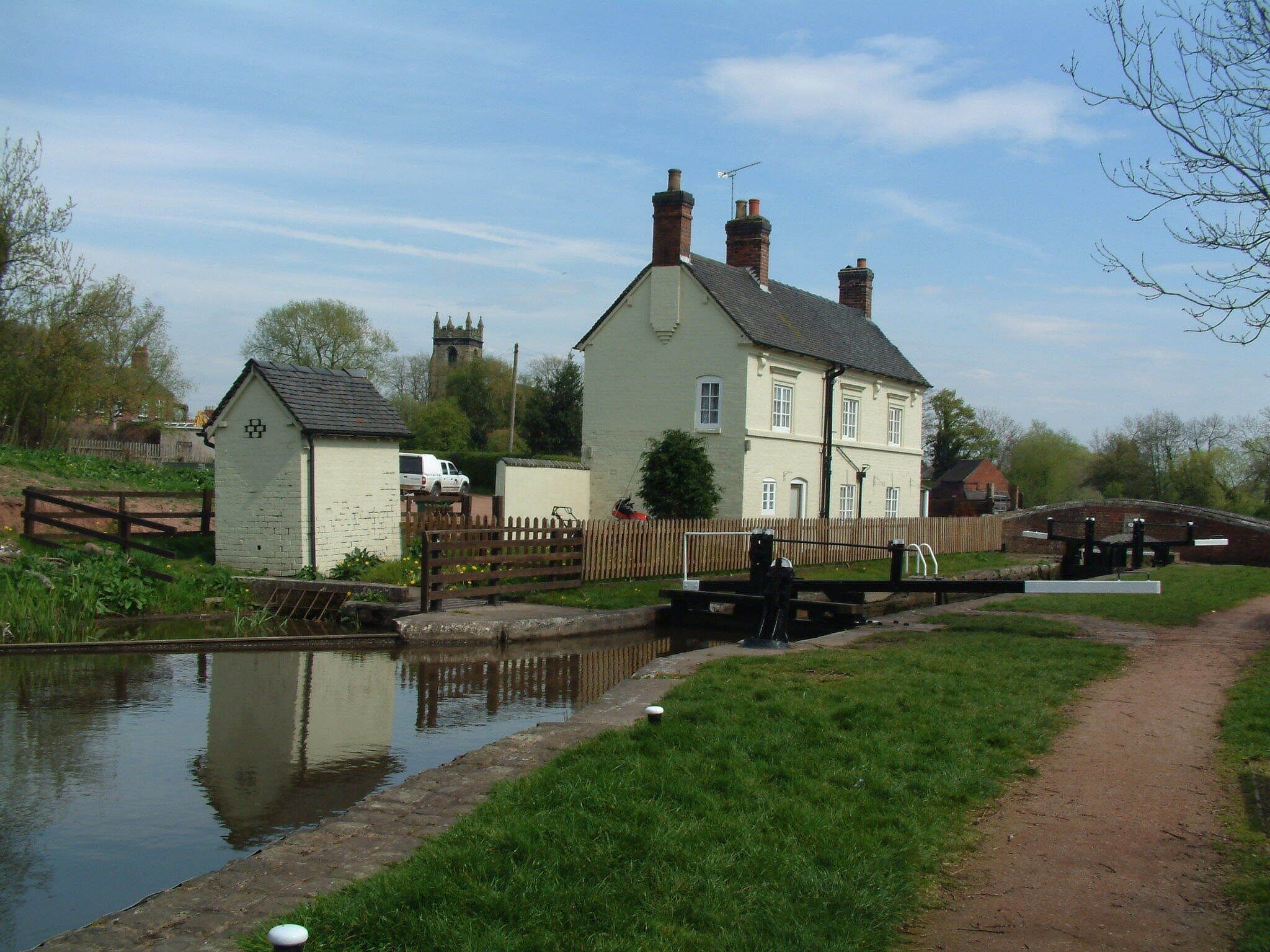 A canal with a lock, a white house, and a church tower in the background.