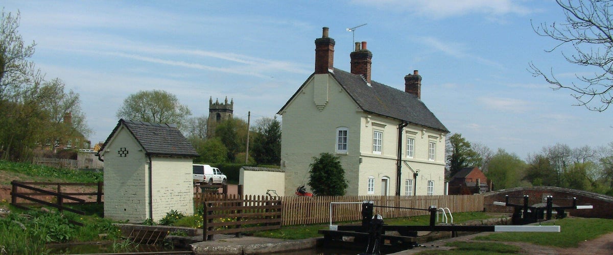 A canal with a lock, a white house, and a church tower in the background.