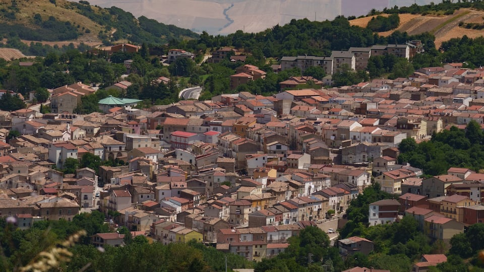 A densely packed town with red-tiled roofs, surrounded by greenery and hills.
