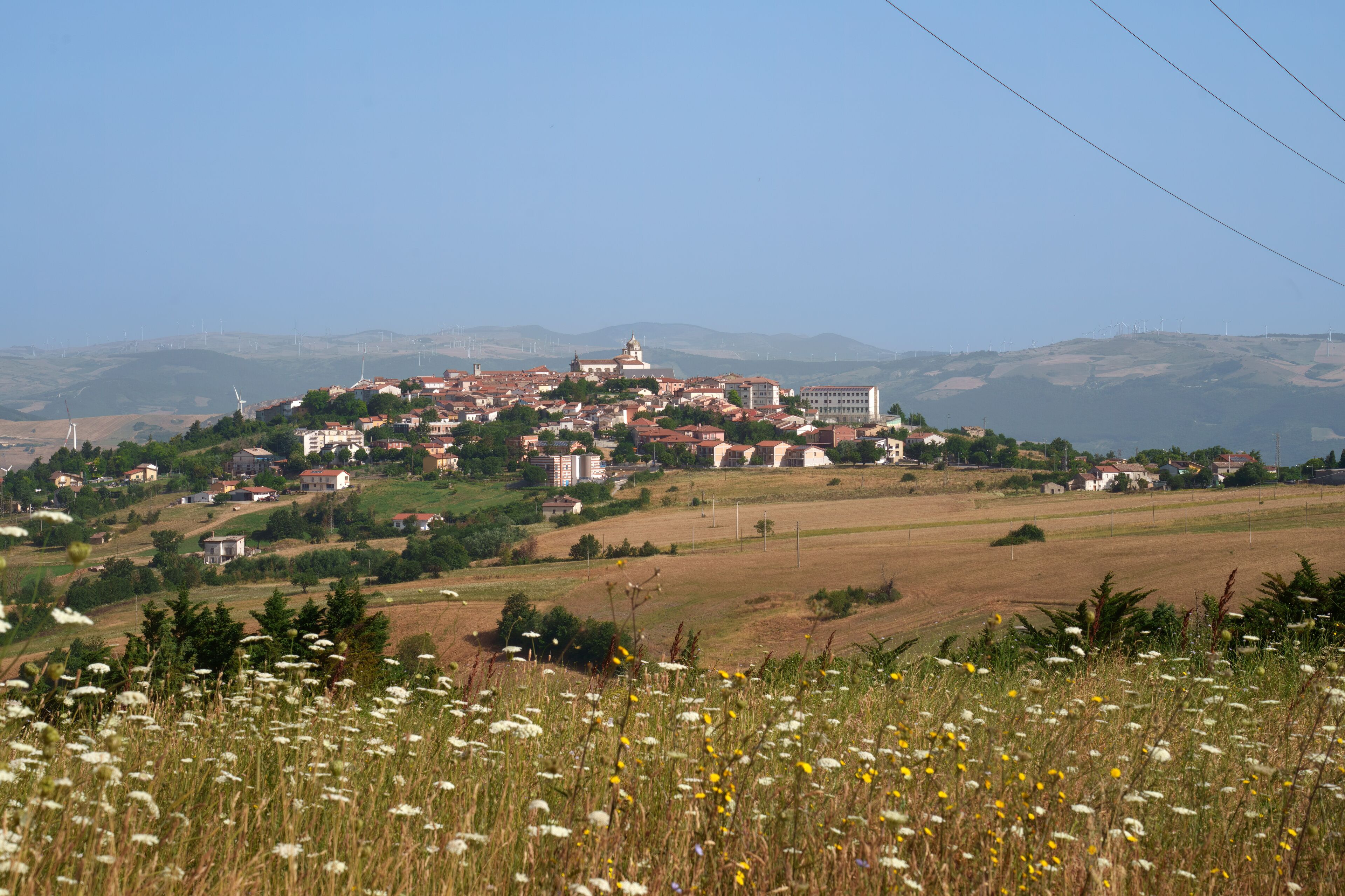 A town on a hill with wind turbines in the background.
