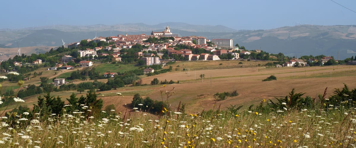 A town on a hill with wind turbines in the background.