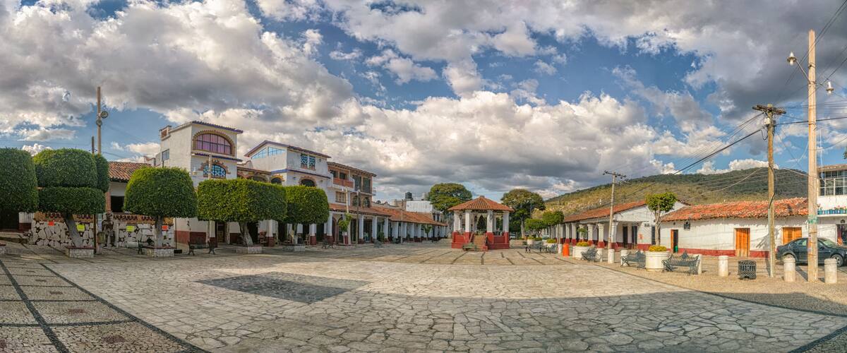 A cobblestone plaza with traditional buildings, a gazebo, and a clear sky.