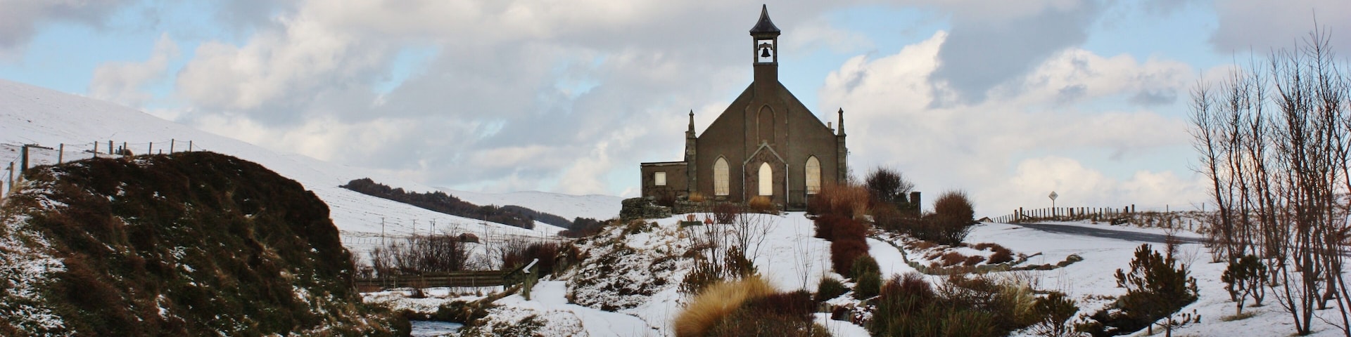 Una iglesia en una colina con un paisaje nevado y un río en primer plano.