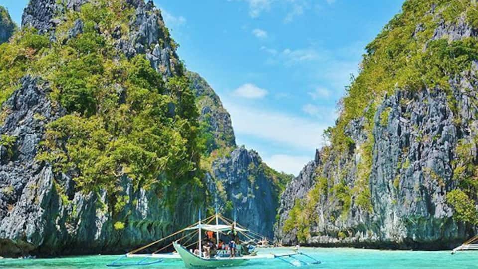 Um barco em águas turquesa, cercado por falésias rochosas e vegetação exuberante.
