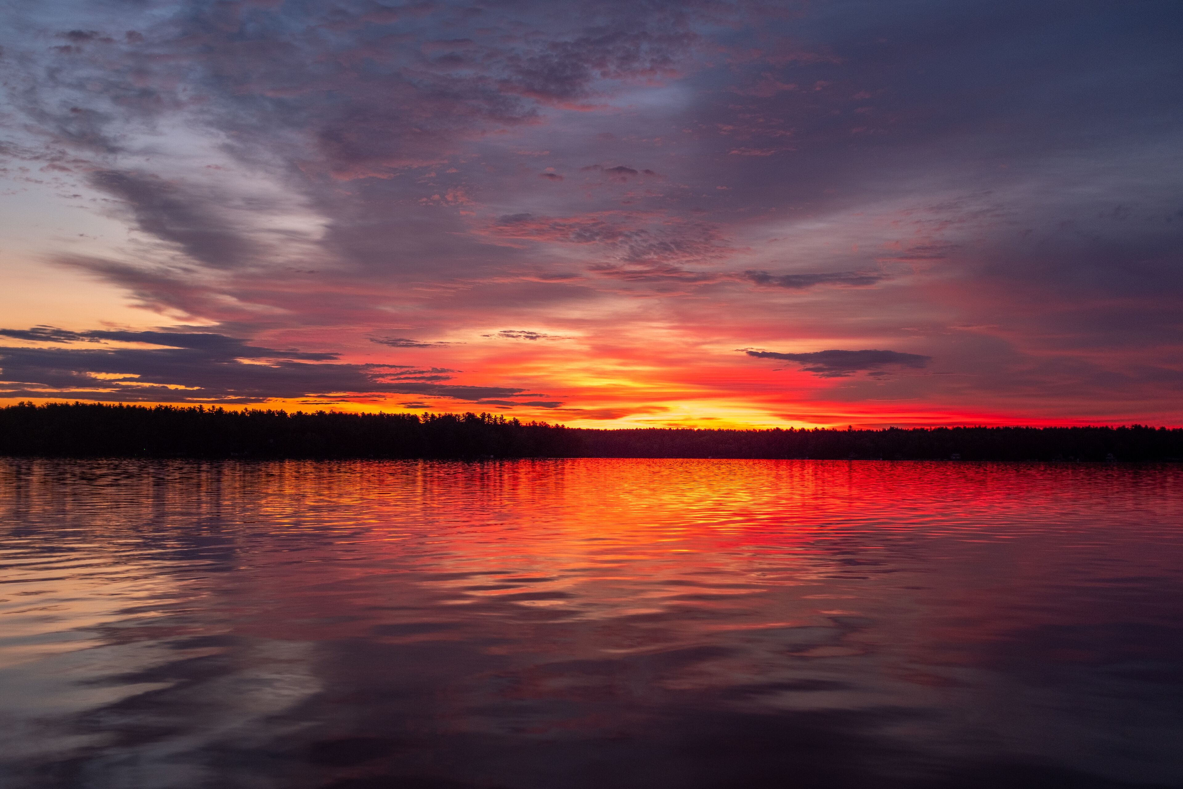 A sunset over a lake with a forest silhouette.