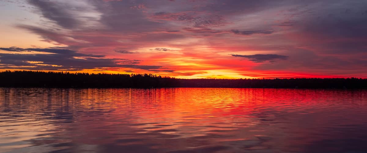 A sunset over a lake with a forest silhouette.