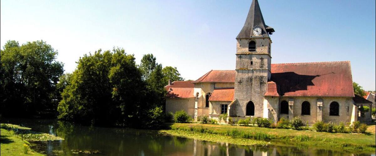 A church with a tall tower and a pond in front.