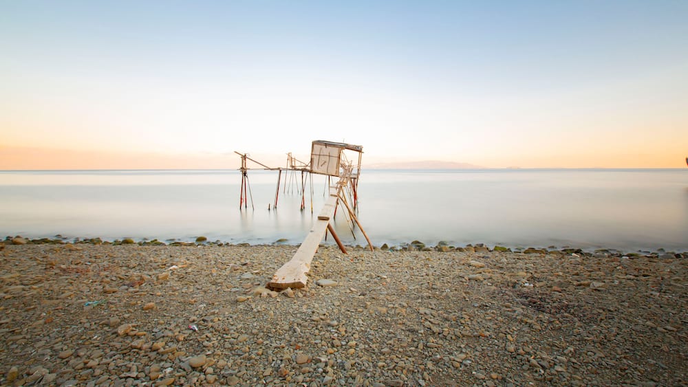 Une plage de galets avec une structure en bois qui s’avance dans une eau calme.