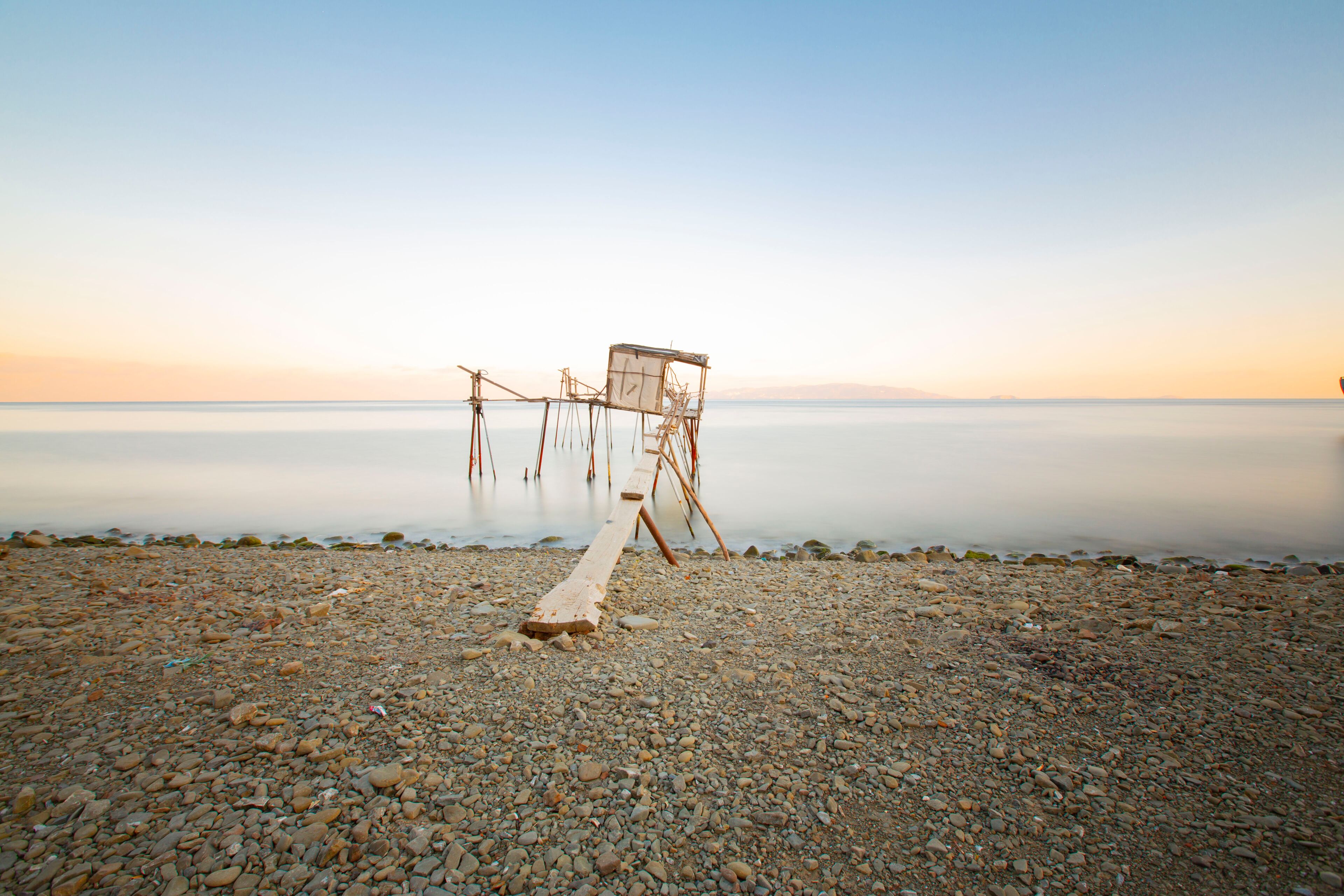 A pebbled beach with a wooden structure extending into calm water.
