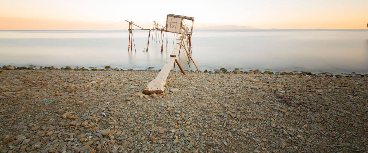 A pebbled beach with a wooden structure extending into calm water.