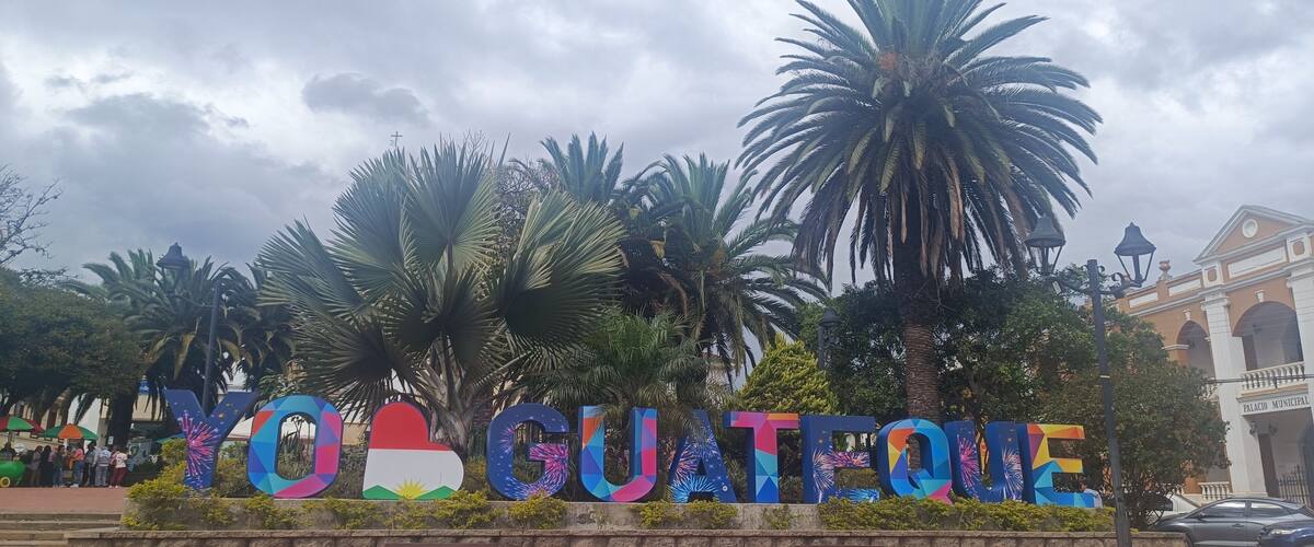 A colorful sign with the text 'YO GUATIQUE' surrounded by palm trees and a building in the background.