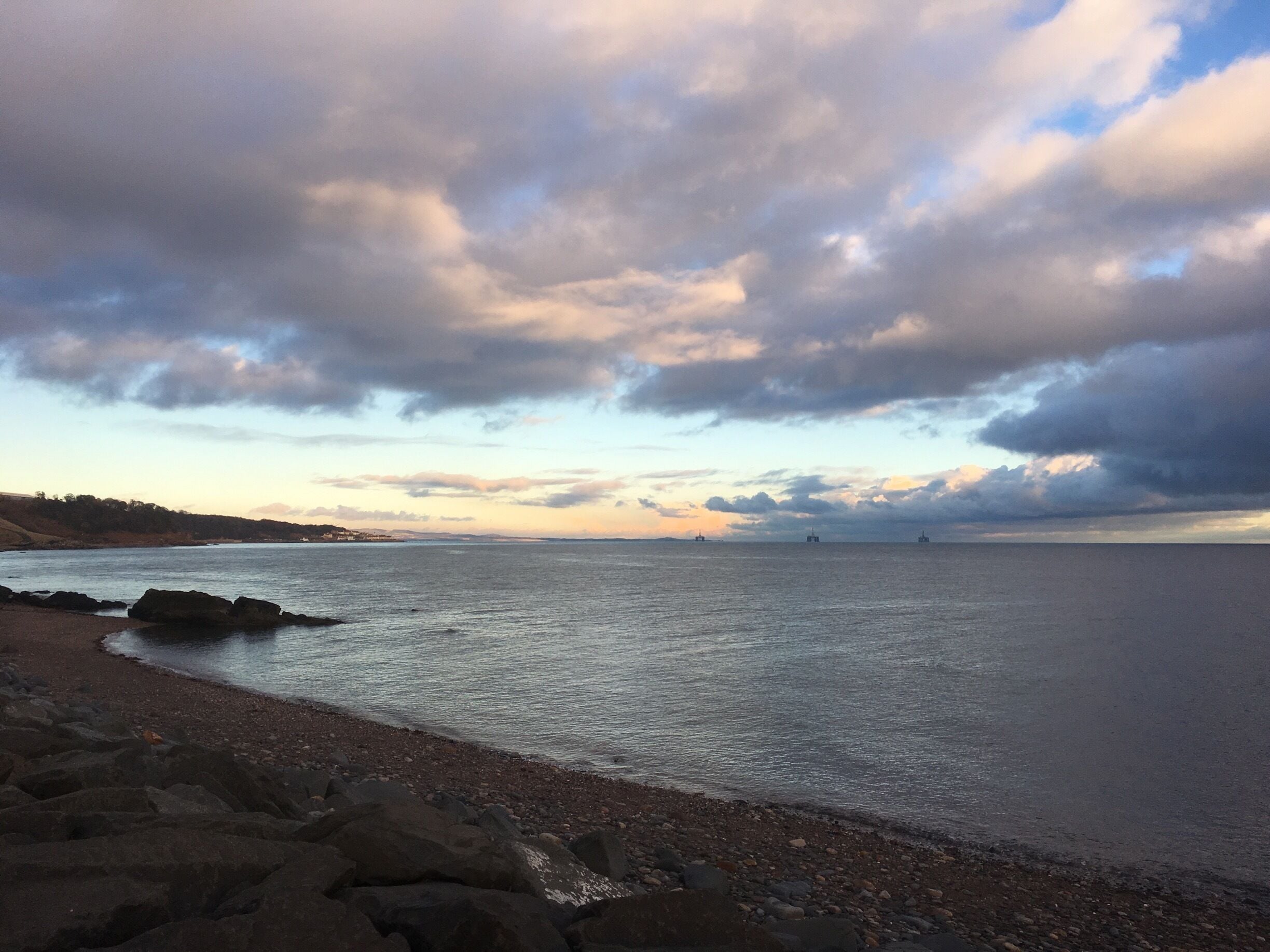 A coastal landscape with a rocky shoreline, calm sea, and a cloudy sky.