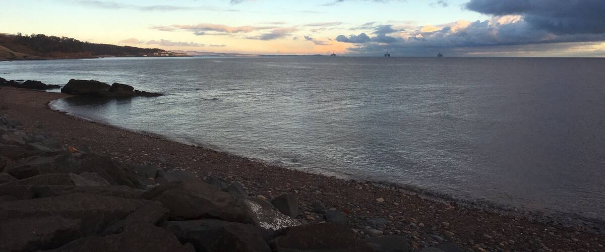 A coastal landscape with a rocky shoreline, calm sea, and a cloudy sky.