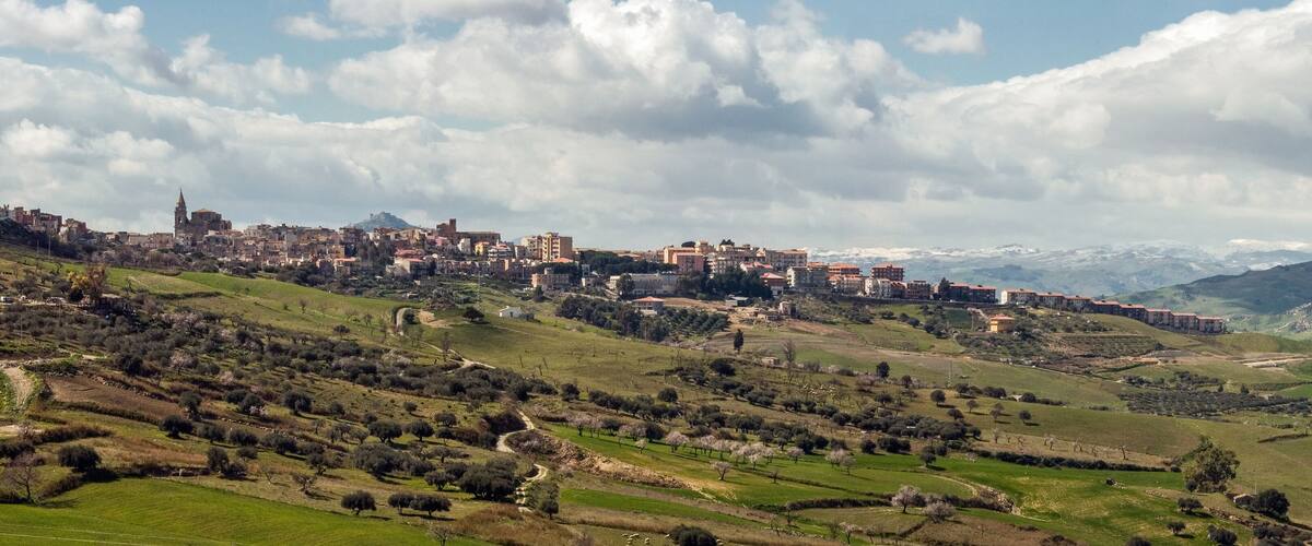 A town on a hillside with a prominent church, surrounded by green fields and mountains in the background.