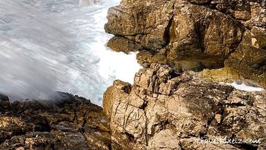 Um castelo à beira-mar com vista para o oceano, falésias rochosas e céu claro.