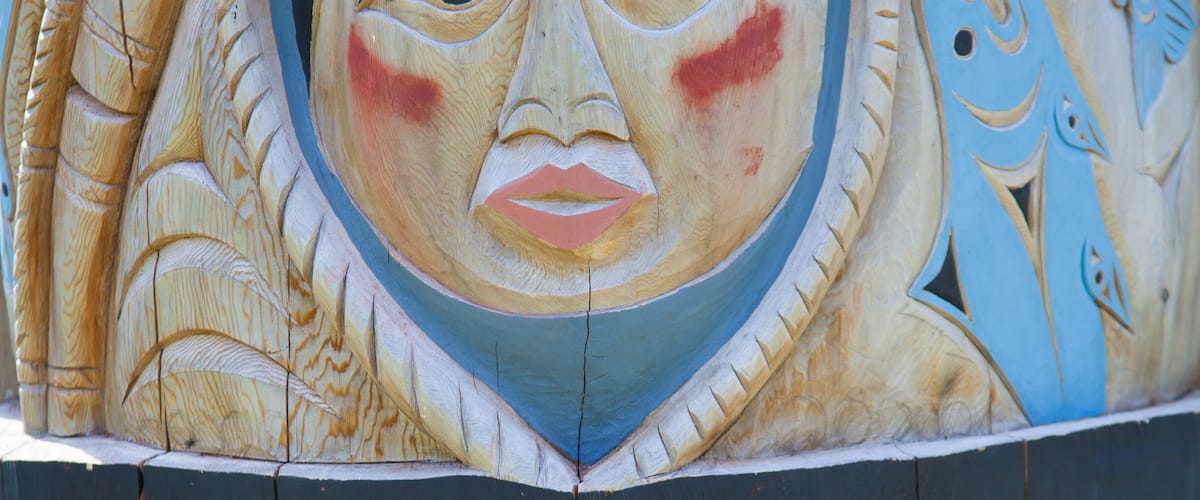 A wooden carving with a face, fish patterns, and a black and red design.
