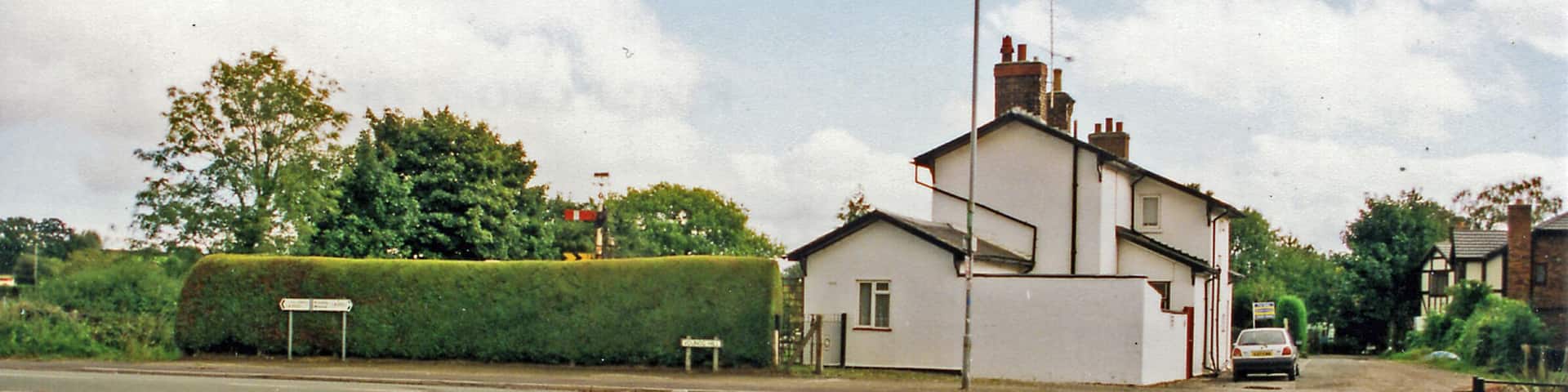 A residential street with a white house, a hedge, and a parked car.