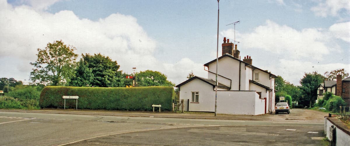 A residential street with a white house, a hedge, and a parked car.