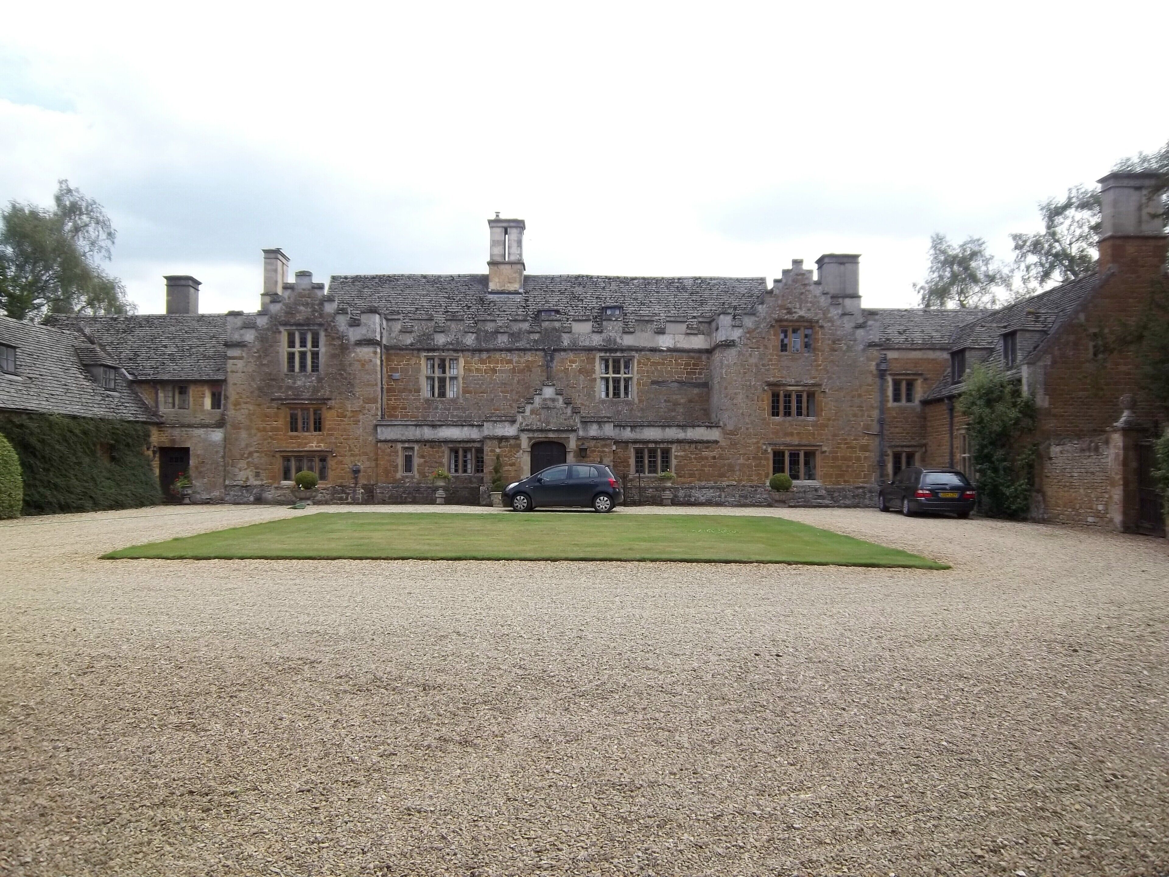 A large stone building with a gravel driveway and parked cars.