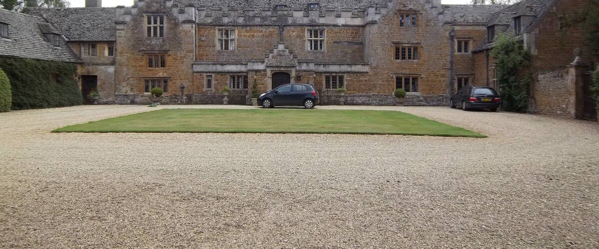 A large stone building with a gravel driveway and parked cars.