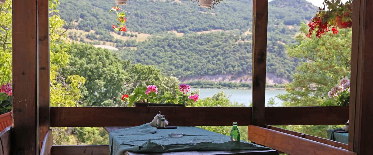 A wooden deck with a table and chairs overlooking a scenic landscape with hills and a body of water.