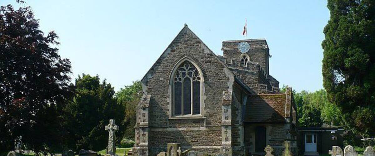 A stone church with a clock tower, surrounded by a cemetery with numerous gravestones.