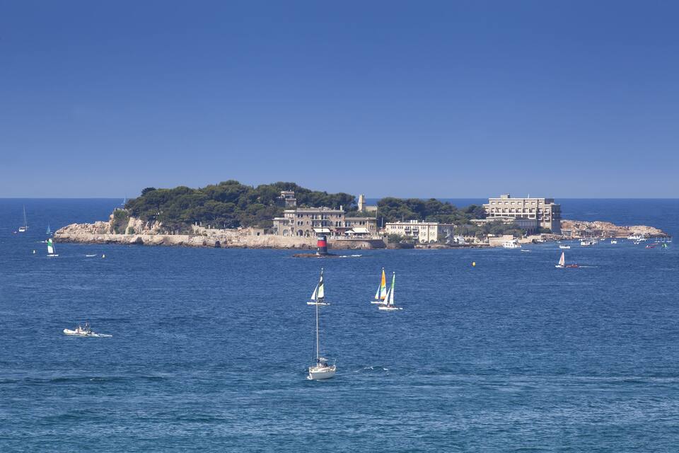 A coastal town with a prominent building on a small island, surrounded by calm waters with several sailboats.