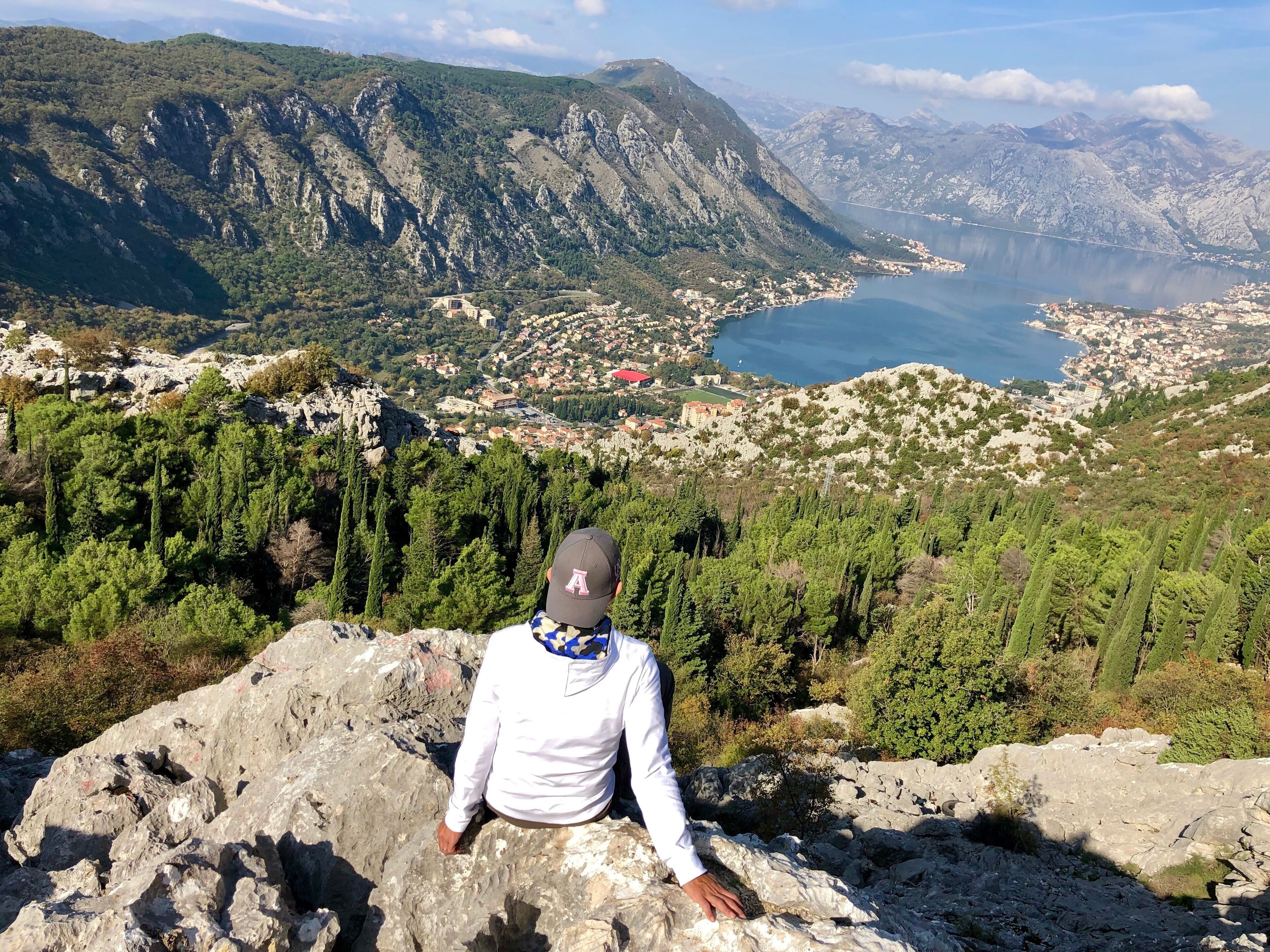A person sitting on a rocky outcrop overlooking a coastal town and mountains.
