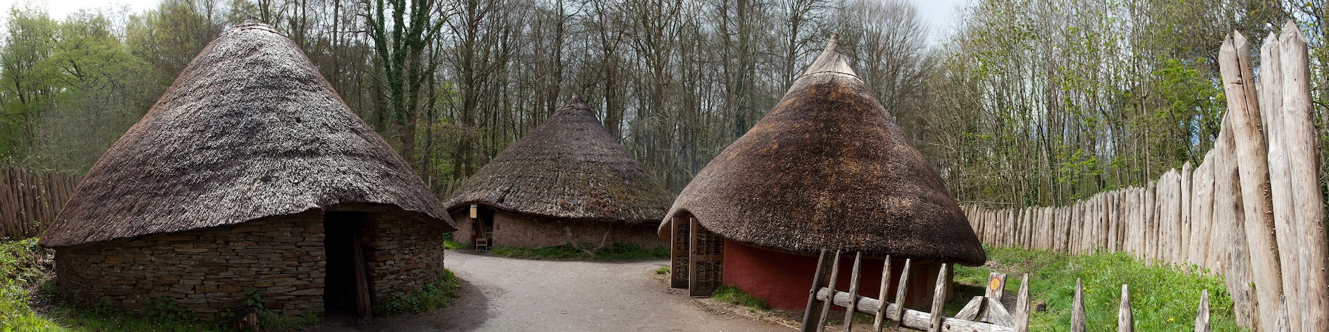 Cabanas de palha em área arborizada, com um caminho de terra.
